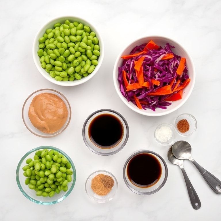 Overhead shot of shelled edamame, shredded red cabbage, julienned carrots, sliced cucumbers, bell pepper strips, and chopped cilantro in small prep bowls with measuring spoons and cups against white marble.