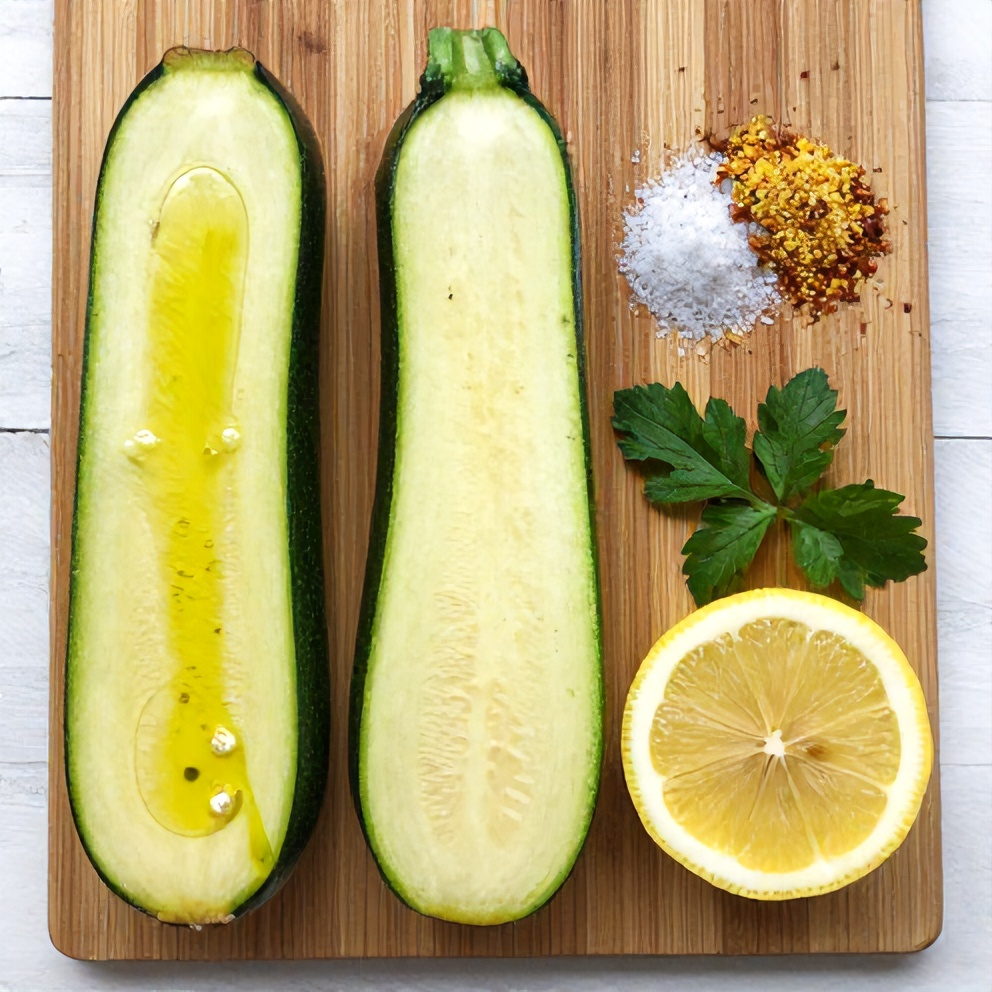 Zucchini, olive oil, salt, pepper, garlic powder, lemon slices, and fresh herbs on a wooden board